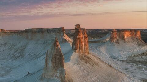 White chalk cliffs and rock formations under a soft pink sky at low sun